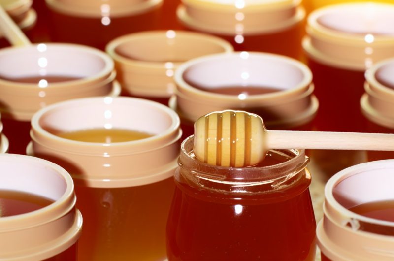 Des pots de miel avec une cuillère à miel, certains miels semblent plus épais et d'autres plus liquides.