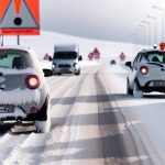 Des voitures coincées sur une route enneigée et verglacée, avec des panneaux de signalisation indiquant les départements en vigilance orange.