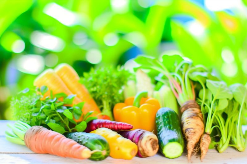 Un assortiment de légumes frais et colorés, comme le brocoli, les épinards, les tomates, les poivrons, les carottes, les choux, les concombres et les avocats, disposés de manière attrayante sur une table en bois.