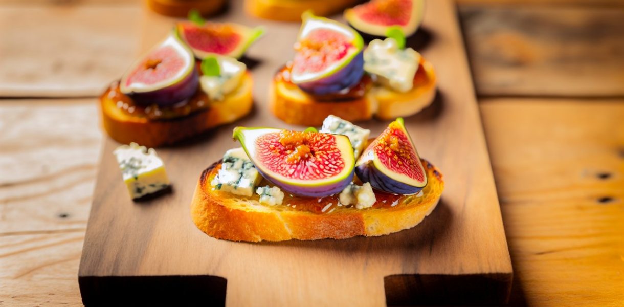 Des crostini garnis de figues fraîches et de fromage bleu disposés de manière appétissante sur une planche à découper en bois.