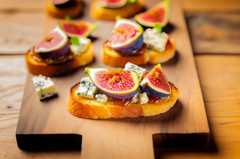 Des crostini garnis de figues fraîches et de fromage bleu disposés de manière appétissante sur une planche à découper en bois.