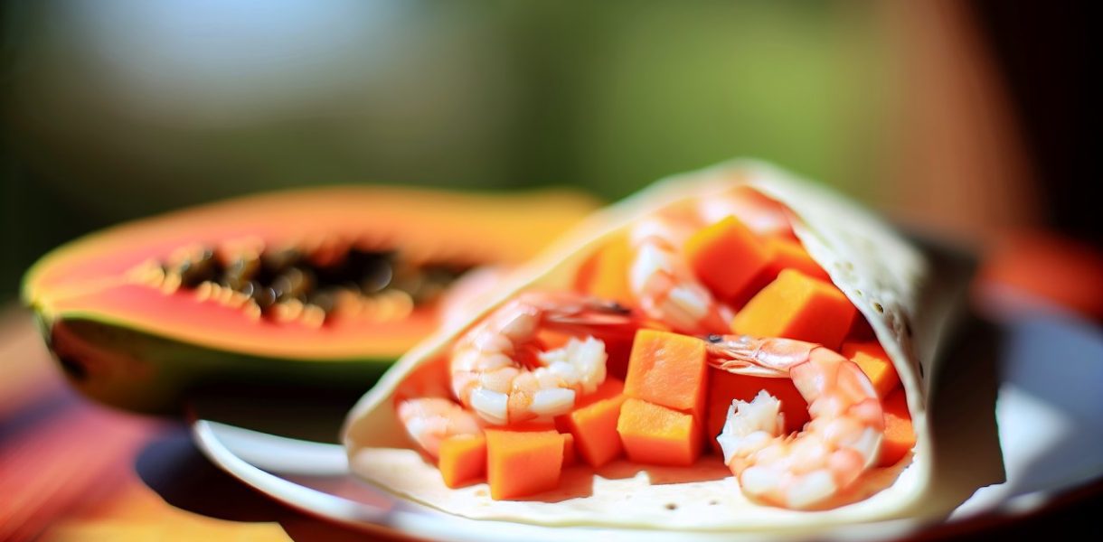Un wrap ouvert garni de crevettes et de morceaux de papaye sur une table exotique.