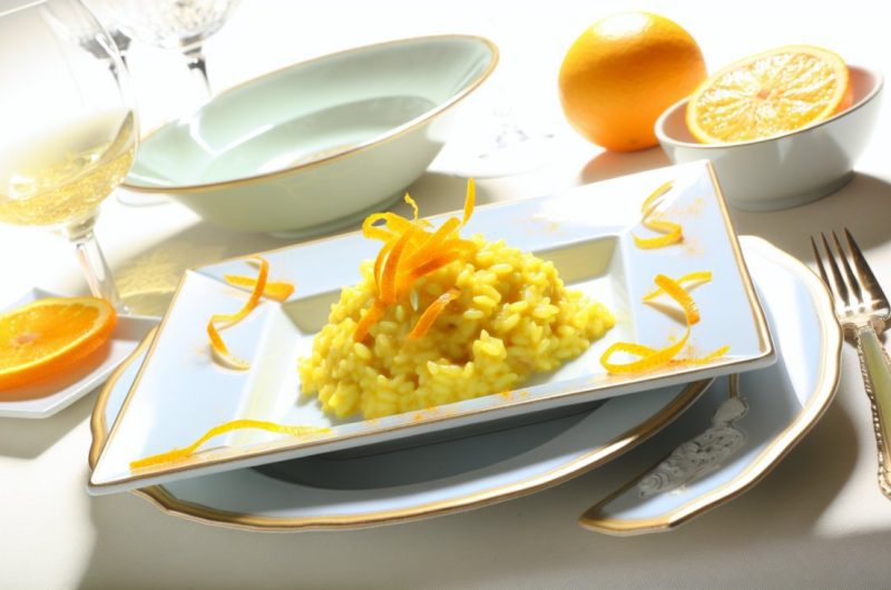 Un plat de risotto au safran garni de zestes d'agrumes, présenté de manière appétissante sur une table bien dressée.